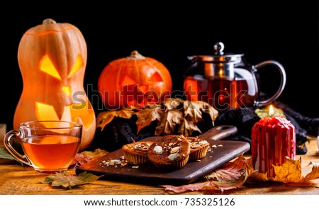 Photo of halloween pumpkins, cakes, cup of tea on black background