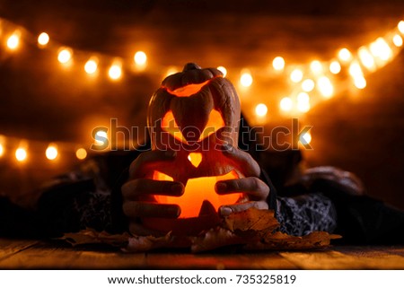 Halloween background with pumpkin and witch hands on wooden table against grunge bokeh lights background