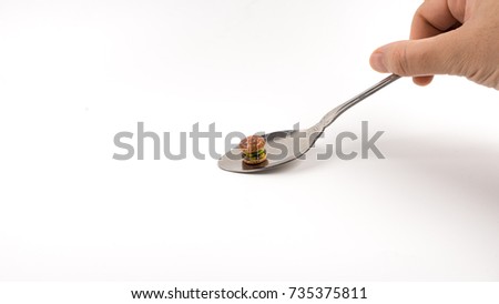 Mini burger on a stainless steel teaspoon. The concept of small portion consumption. Isolated on white background. Slightly de-focused and close-up shot. Copy space.