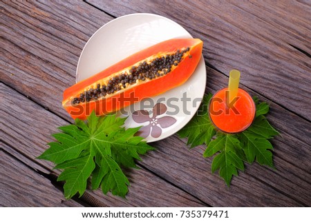 Papaya juice in glass with fresh papaya fruit and leaf on wooden table