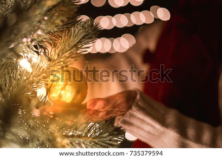 Female hanging gold Christmas ball on tree with bokeh lights background.