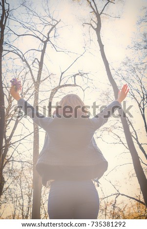 Girl holding bouquet of flowers with arms wide open in nature.