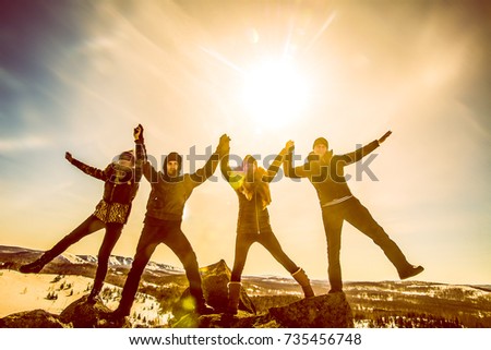 sun light fall on the friends. Friends holding hands and have fun on flank of hill. team of young people outdoor winter setting. Jumping in joy! hands up. sunny winter day. 