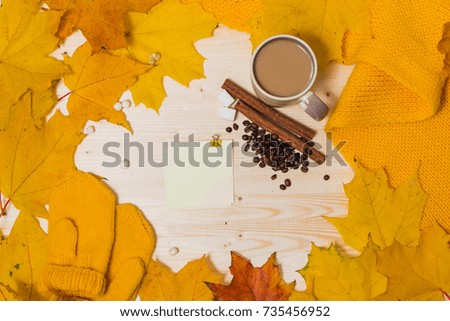 autumn composition - sticker on wooden table orange and yellow leaves, mittens, scarf, cup, coffee beans and cinnamon