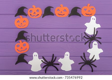 Halloween round frame with different paper silhouettes of pumpkins, hats, ghosts and spiders on a purple wooden table. Halloween celebration. Copy space for greetings