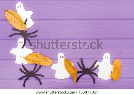 The ghosts and spiders different paper silhouettes with autumn leaves made of halloween corner frame on a purple wooden table. Halloween celebration. Copy space for greetings