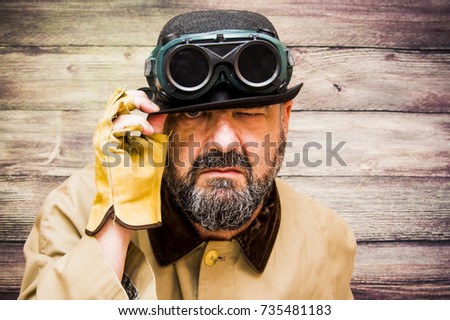 Man with beard, bowler, raincoat and some strange futuristic glasses over wooden background