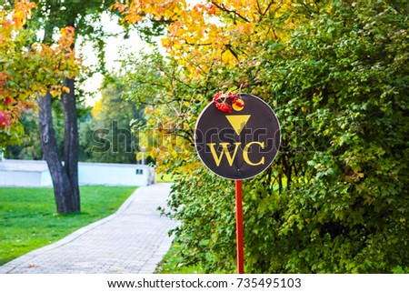 Water closet sign in the park decorated with red berries and autumn trees in the background