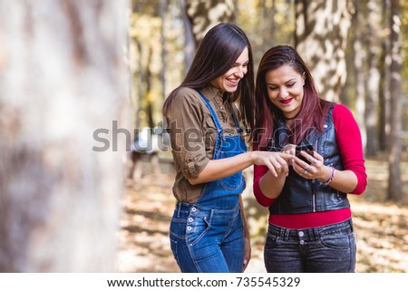 Two pretty girls laughing and watching in the cell phone.