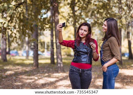 Two pretty girls having fun and taking selfie in the park.