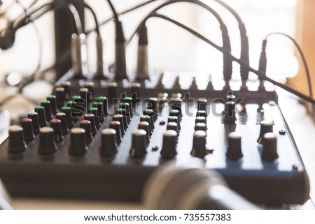 Knobs of an audio mixer in focus, with cables and a microphone nearby.
