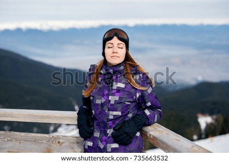Close up of young beautiful girl standing near the fence in winter clothes with eyes closed.