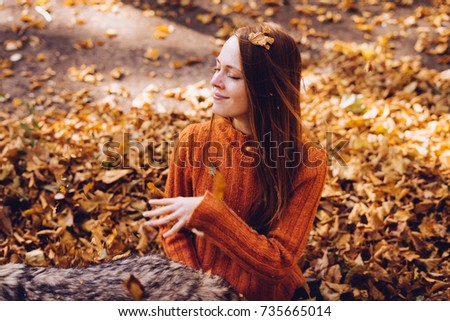 happy smiling red-haired girl sitting around yellow and golden autumn leaves with a dog