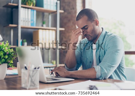 Stressed tired freelancer is having headache and thinking how to finish his work. He is in a casual smart, sitting and suffering at his home office, holding the nose bridge, massaging it Royalty-Free Stock Photo #735692464
