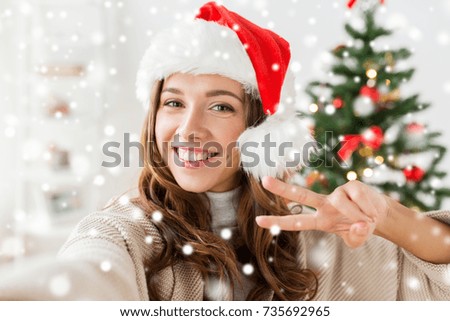 winter holidays and people concept - happy young woman in santa hat taking selfie over christmas tree at home over snow