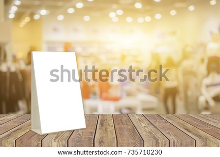 Empty brown wooden table and fashion shoe shop interior with Mock up Menu frame in shopping mall,Stand for booklets with white sheets of paper acrylic tent card on business blurred background