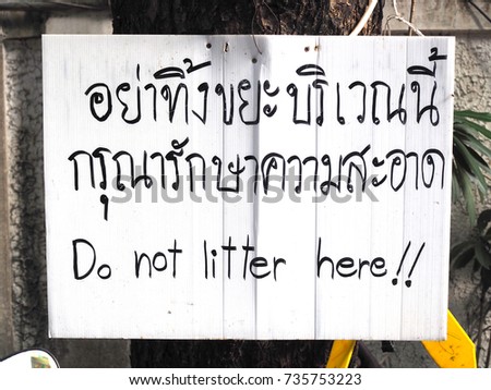 Black handwritten text sign “Please do not throw the trash here” both in Thai and English language, on old weathered white corrugated board, attached on electrical pole
