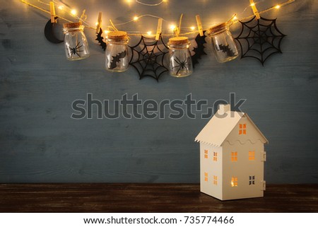 Halloween holiday concept. Mysterious house with lights in front of masson jars with spiders, baths and wooden decorations.