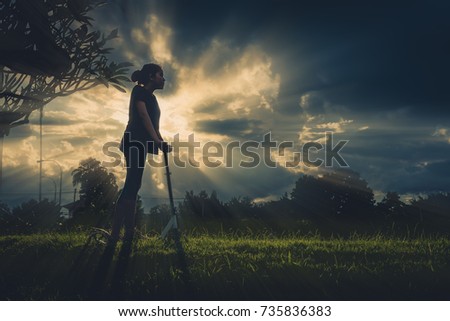 vintage tone silhouette image of Asian girl playing scooter on grass field.