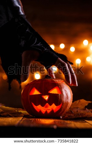 Image of halloween background with pumpkin and witch hand on wooden table against grunge bokeh lights background