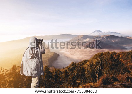 Asian male photographer in coat shooting photos while standing near Mount Bromo, is an active volcano and part of the Tengger massif, in East Java, Indonesia. And with copy space area for your text.