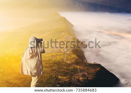 Asian male photographer in coat shooting photos while standing near Mount Bromo, is an active volcano and part of the Tengger massif, in East Java, Indonesia. And with copy space area for your text.
