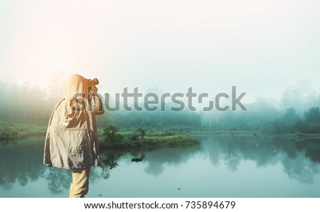 Asian male photographer in coat shooting photos while standing in Forest with space area for your text.