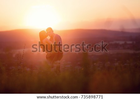 man and girl in love romantic lovers kissing, hugging at sunset, sunrise on the background of mountains and fog, sun, clouds in fiery red, orange colors. 