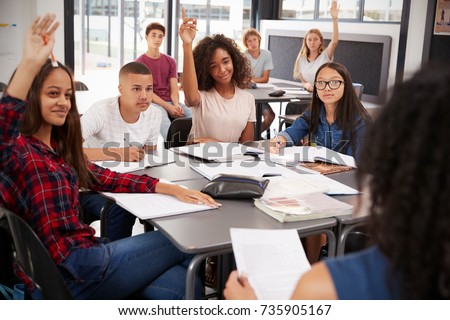 High school kids raise hands, teacher sitting at their desk Royalty-Free Stock Photo #735905167