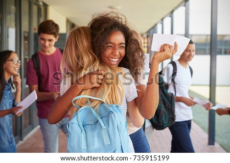 Two girls celebrating exam results in school corridor Royalty-Free Stock Photo #735915199