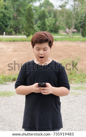 Technology in Daily Life.  asia boy wearing black T shirt  in at garden, looks down,  on cell phone.