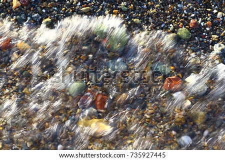 Wave covers colorful pebbles on the beach