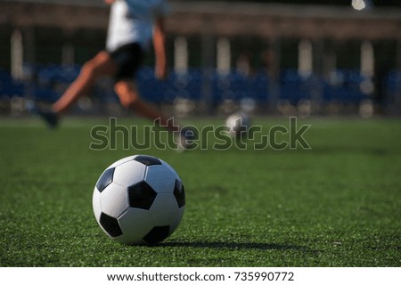 Traditional soccer ball on green grass, silhouettes of playing people on background. Football game, outdoors activity, summer sunny day.