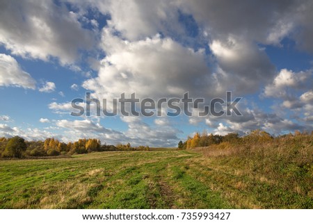 Colorful autumn landscape with a field in hilly terrain. Evening. The sky with heavy white clouds. Picture, Wallpapers, calendar.