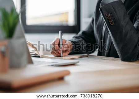 close-up partial view of businessman taking notes in notebook at workplace