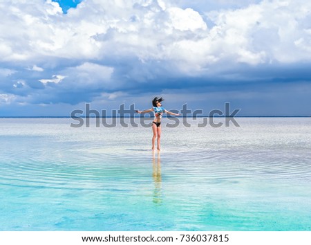 Cheerful bright brunette girl jumps on the water for a photo. A heavenly place, beautiful seascape, clouds on the horizon. Girl in swimsuit makes a jump on salty water of saline.