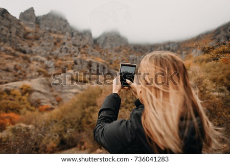 A young girl takes photos of a autumn mountain landscape. Foggy day.