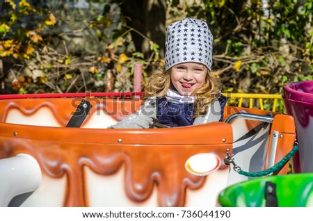 A small charming girl goes for a drive in an amusement park on a merry-go-round, in a large coffee mug, on a sunny autumn day