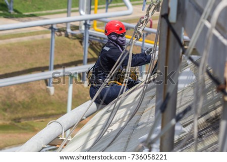 Male worker sitting on fire water tube rope access of inspection storage tank