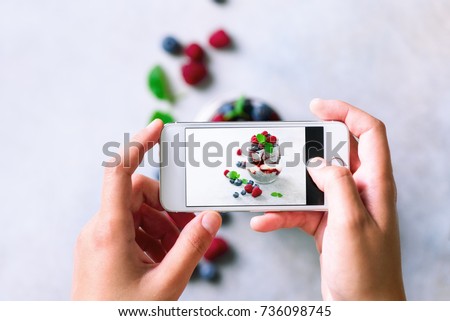 Girl is taking photos of breakfast, chia pudding with berries to mobile phone. Social media, instagram concept. Copy space, top view