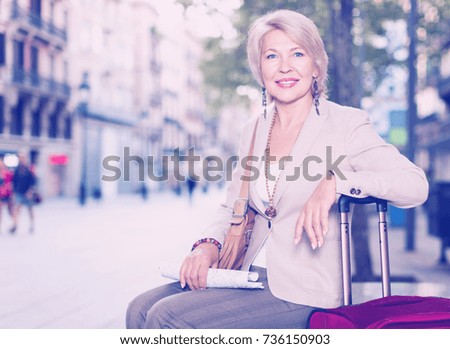 Mature female tourist is sitting with map on the street outdoor.