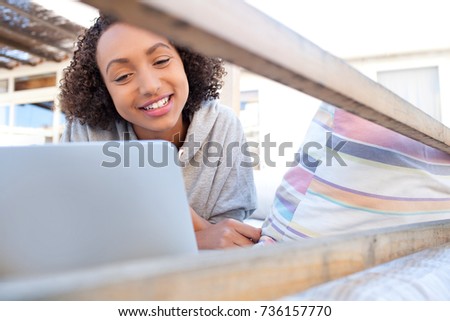 Portrait of teenager african american student girl laying on home garden bed using a laptop computer, smiling joyful outdoors. Young black woman using technology, recreation lifestyle home exterior.
