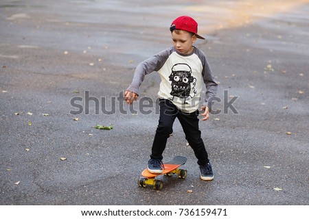 Little urban boy with a penny skateboard. Young kid riding in the park on a skateboard. City style. Urban kids. Child learns to ride a penny board