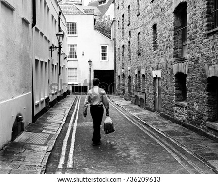 Man Walking With Shopping Bag Down Narrow English Street, Black and White Photography