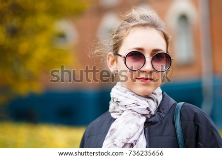Young female student standing near college building in autumn. Education background with student girl and copy space