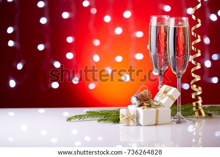 Two glasses with champange, fir tree branch, gift boxes and christmas decorations on a red background with lights of garland.  New year and Christmas.