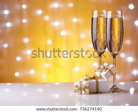 Two glasses with champange and gift boxes on a yellow background with lights of garland.