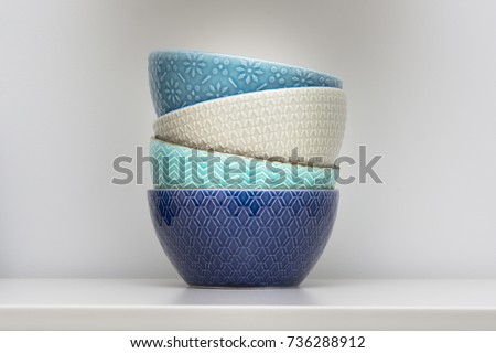 Four designer ceramic bowls in different colors stacked together. Bowls on white background in restaurant cafe. Blue, turquoise, grey and dark blue bowls.