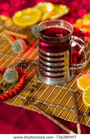 Mulled wine in metal cup holder with orange and chocolate sticks and biscuits, marmalade green ball and candy, bokeh

