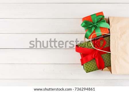 Colored handmade christmas gifts in craft paper bag on white wood table background. Copy space, top view